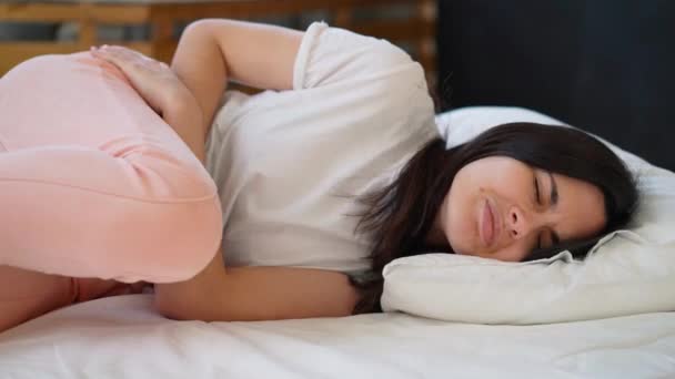 Junge Frau leidet unter Bauchschmerzen, während sie zu Hause im Bett sitzt — Stockvideo