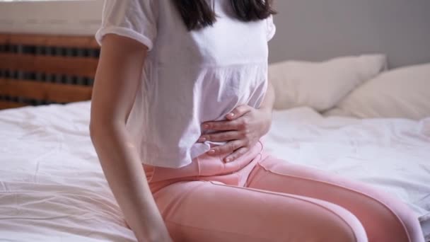 Mladá žena trpí bolestí břicha, zatímco sedí doma na posteli — Stock video