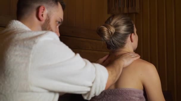 Un hombre hace un masaje de espalda y cuello hermosa mujer en la sauna, baño . — Vídeo de stock