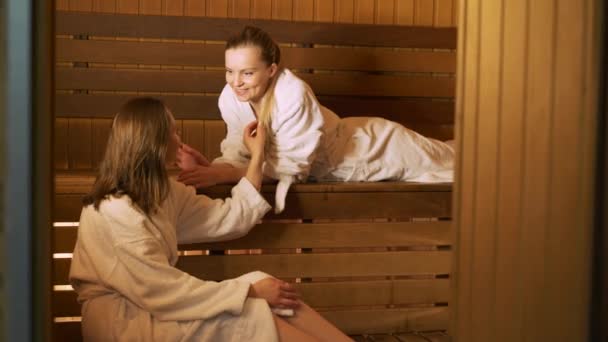 Zwei glückliche Frauen im Gespräch miteinander in einer Sauna — Stockvideo