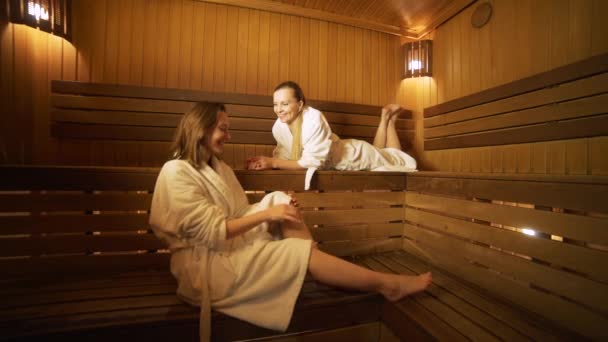 Zwei glückliche Frauen im Gespräch miteinander in einer Sauna — Stockvideo