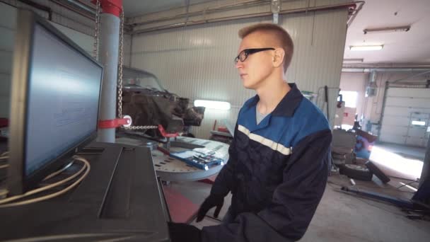 Ritratto di un giovane bellissimo meccanico in officina, sullo sfondo di un'auto rotta. Concetto: riparazione della macchina, diagnosi dei guasti, riparazione specialistica, manutenzione . — Video Stock