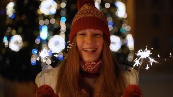 Uma menina segura uma frente de luz de Bengala para a árvore de Natal — Vídeo de Stock