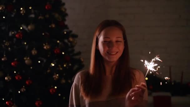 Uma menina segura uma frente de luz de Bengala para a árvore de Natal — Vídeo de Stock