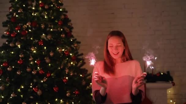 Uma menina segura uma frente de luz de Bengala para a árvore de Natal — Vídeo de Stock