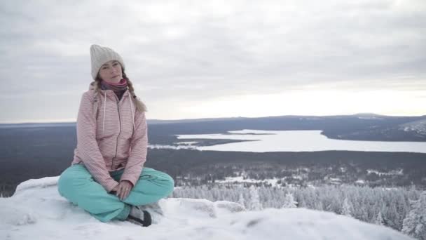 Hermosa chica rubia con coletas sentadas en la cima de la montaña cubierta de nieve — Vídeos de Stock
