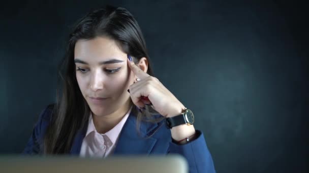 Jeune belle femme d'affaires assise à une table avec un ordinateur portable. Le soir, une pigiste travaille à distance. Cours de formation en ligne, livres de lecture, regarder des vidéos en ligne . — Video