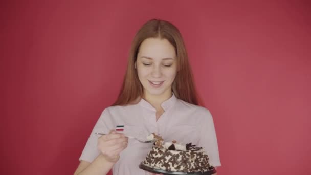 Aranyos lány étkezési kanállal torta, élvezve finom süteményeket, piros háttér — Stock videók