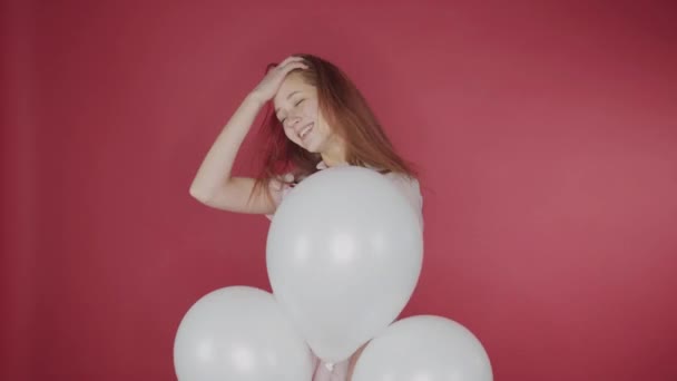 Födelsedag, alla hjärtans dag koncept. Lycklig tjej som håller ett gäng ballonger på en röd bakgrund, är flickan lycklig — Stockvideo