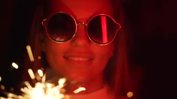 Une fille tenant un scintillant, néon rouge. Jeune belle femme avec des lunettes tenant un feu de bengale brûlant . — Video