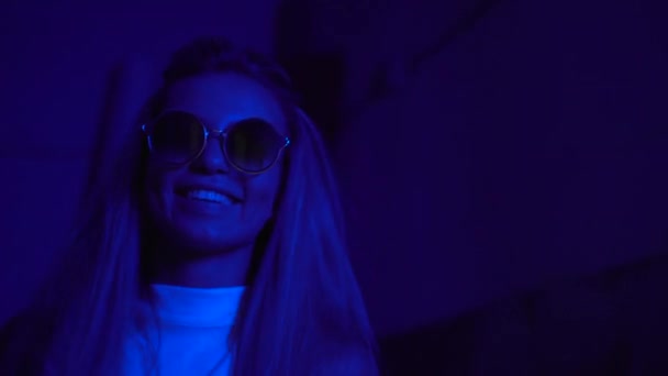 Mladá hezká dívka poblíž zářící neonové světla města v noci. Hipster teenager s brýlemi a krásnými objektivy — Stock video