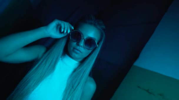 Menina bonita jovem perto de luzes de néon brilhantes da cidade à noite. Hipster adolescente em óculos e lentes bonitas — Vídeo de Stock