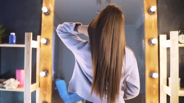 Hermoso cabello limpio y bien cuidado de una mujer joven después de un procedimiento de Botox en un salón de belleza. La chica está contenta con el resultado, contra el espejo — Vídeos de Stock