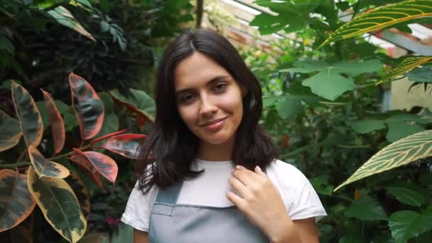 Garota jardineiro olha para a câmera e sorri, segurando uma lata de rega para regar flores . — Vídeo de Stock