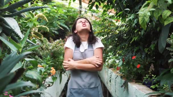 The girl in the greenhouse in the apron, itching from pollen plants. Allergic to flowers — Stock Video