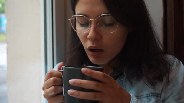 窓でコーヒーを飲むブルネットの女性 — ストック動画