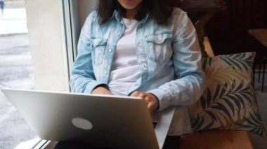 Kız bir kafede bir pencerenin önünde bir dizüstü bilgisayar çalışır. Genç güzel iş kadın karanlık bir kafede oturur ve onu laptop sert çalışıyor.