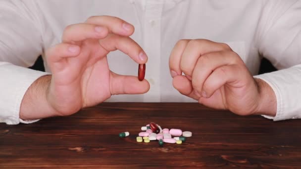 O médico pega uma pílula de uma pilha de dispersos. O viciado escolhe um comprimido. Os comprimidos estão espalhados na mesa . — Vídeo de Stock