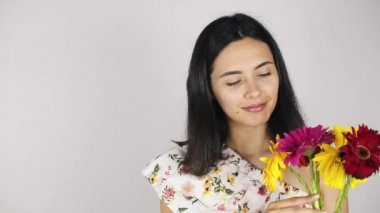 Kız bir buket çiçek ile yakın yüz. Gri arka planda bir buket çiçek koklayan güzel bir genç kadının portresi