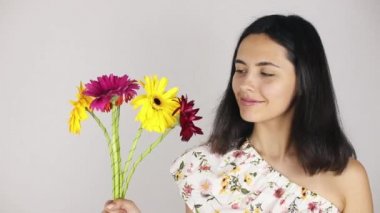 Kız bir buket çiçek ile yakın yüz. Gri arka planda bir buket çiçek koklayan güzel bir genç kadının portresi