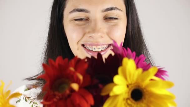 La cara de niña de cerca con un ramo de flores. Retrato de una hermosa joven olfateando un ramo de flores sobre fondo gris — Vídeos de Stock