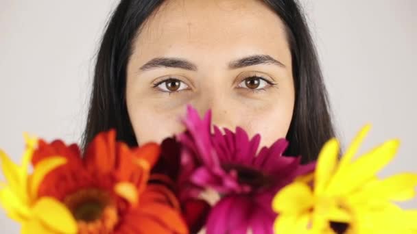 La cara de niña de cerca con un ramo de flores. Retrato de una hermosa joven olfateando un ramo de flores sobre fondo gris — Vídeos de Stock