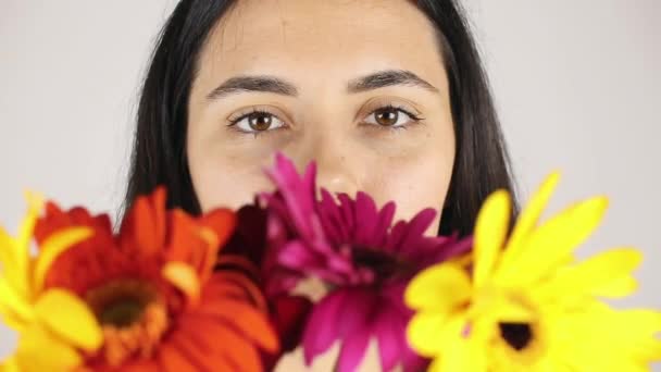 La cara de niña de cerca con un ramo de flores. Retrato de una hermosa joven olfateando un ramo de flores sobre fondo gris — Vídeos de Stock