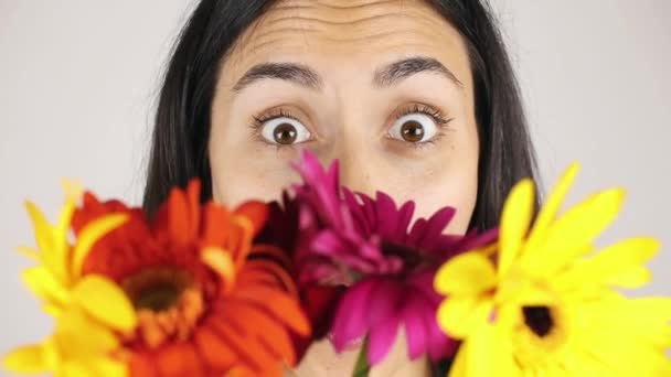 A lány arca közelről egy csokor virágot. Portré egy csinos fiatal nő szippantás egy csokor virágot szürke háttér — Stock videók