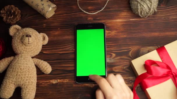 Houten achtergrond. Bovenaanzicht. Zwarte smartphone met groen scherm liggend op de tafel met Kerst vakantie decoratie. — Stockvideo