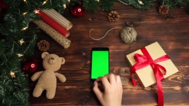 Ahşap arka plan. Üst te. Noel tatili dekorasyonu ile masada yatan yeşil ekranlı siyah akıllı telefon.