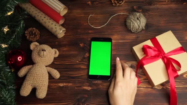 Holzuntergrund. Ansicht von oben. schwarzes Smartphone mit grünem Bildschirm auf dem Tisch mit Weihnachtsdekoration. — Stockvideo