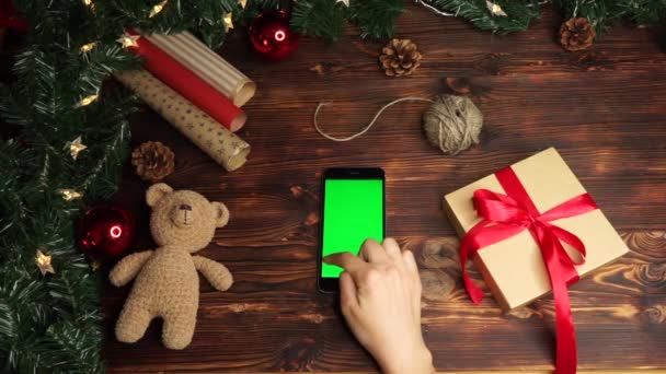 木制背景。顶部视图。黑色智能手机与绿色屏幕躺在桌子上与圣诞节节日装饰. — 图库视频影像