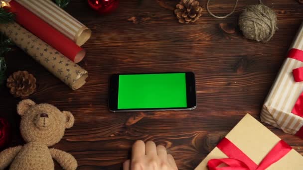 Trä bakgrund. Översta vyn. Svart smartphone med grön skärm liggande på bordet med julhelg dekoration. — Stockvideo