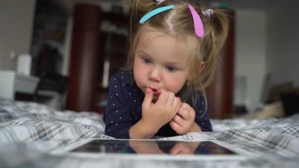 Funny little girl watching cartoons, lying on the bed and picking her nose. — Stock Video