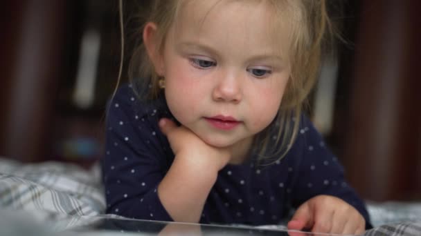 Curiosa niña linda preescolar utilizando tableta digital dispositivo de tecnología que se encuentra en el suelo de la alfombra solo. Pequeño niño mantenga la computadora de la almohadilla de navegación juego de Internet en casa. Concepto de adicción tecnológica infantil . — Vídeos de Stock