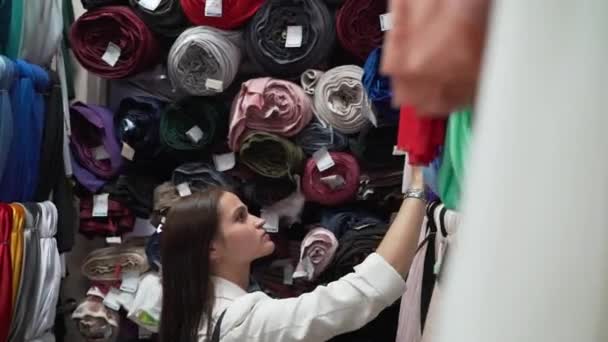 Девушка выбирает ткань в магазине тканей — стоковое видео