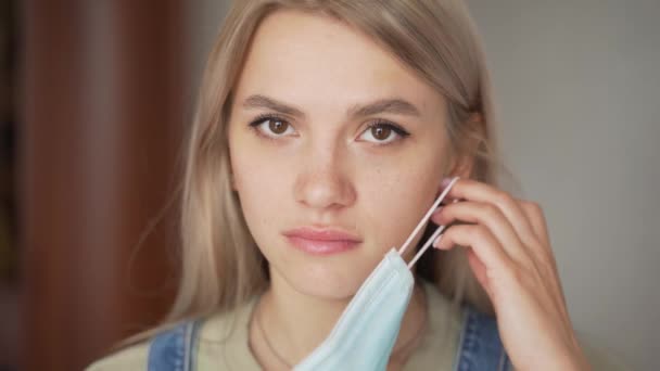 Het meisje zet een medisch masker op van het virus en kijkt naar de camera — Stockvideo