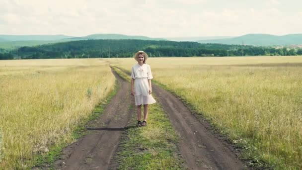 Девушка в платье прогуливаясь по дороге в поле, наслаждаться чистым воздухом. — стоковое видео