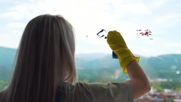 Het blonde meisje in de gele handschoenen wast een vuil raam met een groene spons — Stockvideo