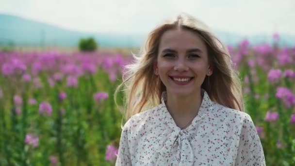 Porträt eines entzückenden blonden Mädchens in einem weißen Kleid, das in einem Feld aus blühendem Tee steht. — Stockvideo