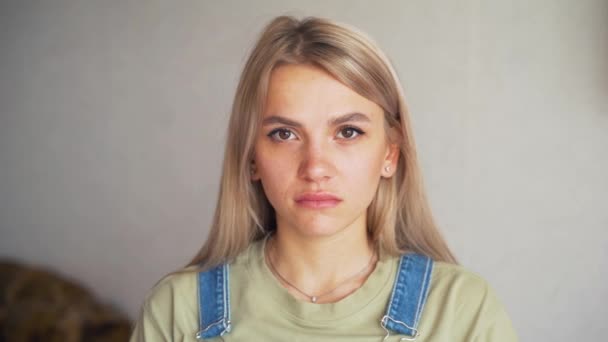 Egy komoly, koncentrált arcú szőke kaukázusi lány portréja, aki egy fehér fal előtt áll — Stock videók