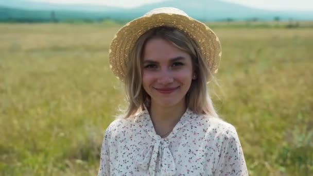 Beautiful blond girl in the white summer dress and hat standing in field, wearing a sunglasses. — Stock Video