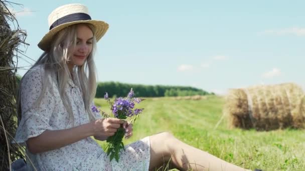 Piękna dziewczyna w białej sukience i kapeluszu, zebrane kwiaty na polu — Wideo stockowe