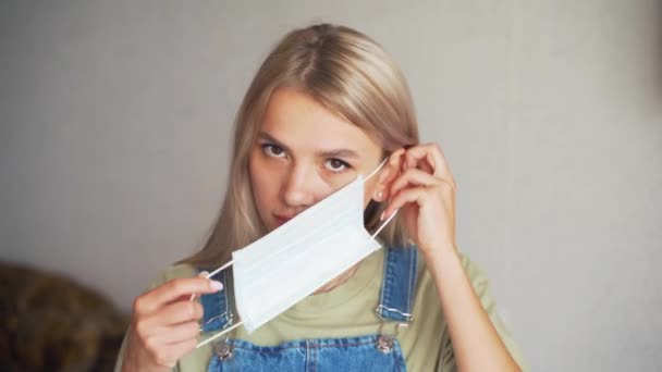 Krásná blondýna dívka nosí ochrannou masku, zatímco v bytě — Stock video