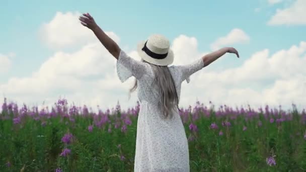 Beautiful woman in a white dress and a hat is dancing in the field with open wide arms. — Stock Video