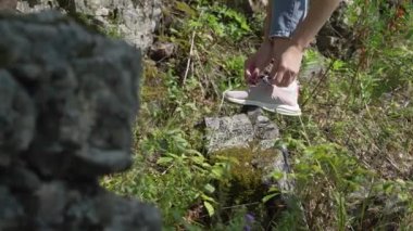 Ormanda bir gezginin ayakkabısına ayakkabı bağlayan bir kızın ellerini yakın plan..