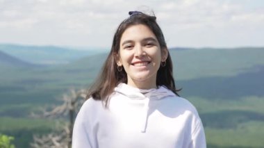 Bir dağın tepesinde durup kameraya bakan gülümseyen bir kızın portresi..