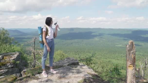 Dívka pije vodu na vrcholu hory po dlouhé cestě na vrchol. — Stock video