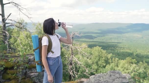 Dívka pije vodu na vrcholu hory po dlouhé cestě na vrchol. — Stock video