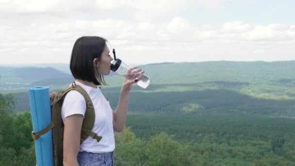 Dziewczyna pije wodę na szczycie góry po długiej podróży na szczyt. — Wideo stockowe